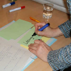 Dialogteilnehmerin schreibt das Wort Lösung auf eine Moderationskarte.