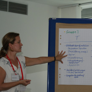 Teilnehmerin steht an der Moderationswand und zeigt auf die Ergebnisse der Arbeitsgruppe 3.