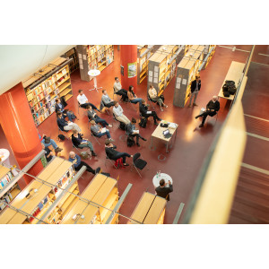 Der Blick geht von oben auf die sitzenden Worshopteilnehmenden und öffnet damit den Blick auf den Ort des Workshops: eine Bibliothek.