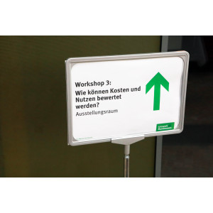 Hinweisschild mit grünem Pfeil zeigt in Richtung Workshop 3: Wir können Kosten und Nutzen bewertet werden ?