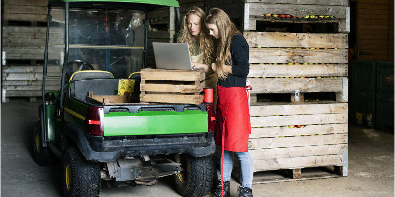 Auf dem Bild sind zwei Frauen auf einem Obstbauerhof zu sehen, die einen Laptop benutzen.