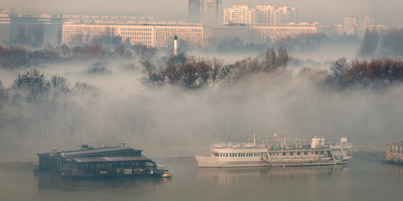 Foto: Nebel über einem Fluss und seinen Uferbereichen. Im Hintergrund sind die Häuser einer Stadt zu sehen.