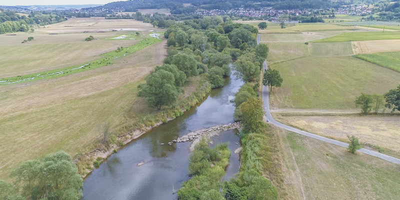 Luftbild der Fulda mit schräg zur Fließrichtung eingebrachten Steinen. Die dadurch abgelenkte Strömung hat bereits eine Erosion des Ufers bewirkt.