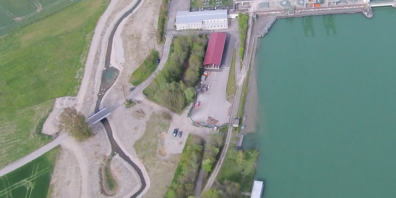 Luftbild des Kraftwerks Gars am Inn, um das ein künstlich angelegtes Umgehungsgewässer für Fische herumführt.