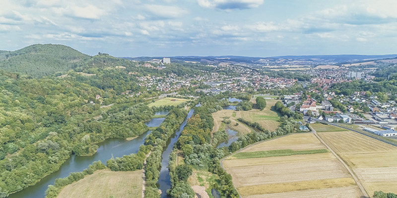 Luftbild der Fulda mit Nebengewässern und großräumigen Auenflächen. Entlang des Gewässers wachsen breite Randstreifen, an die landwirtschaftliche Flächen angrenzen. Im Hintergrund liegen Siedlungsflächen.