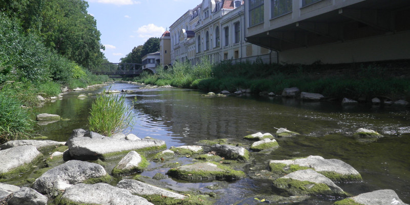 Foto: Ein renaturierter Flussabschnitt mit geradem Flusslauf wird über größere Steine und Blöcke strukturreicher und naturnäher gestaltet. 