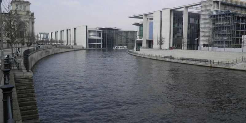 Foto: Die Spree mit Paul-Löbe und Marie-Elisabeth-Lüders-Haus im Hintergrund. Die Uferkante ist betoniert, am Ufer entlang verlaufen Wege. 