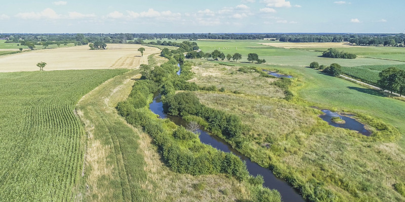 Luftbild der Wümme mit durchgehendem Gehölzsaum, umgeben von landwirtschaftlich genutzten Grün- und Ackerlandflächen.