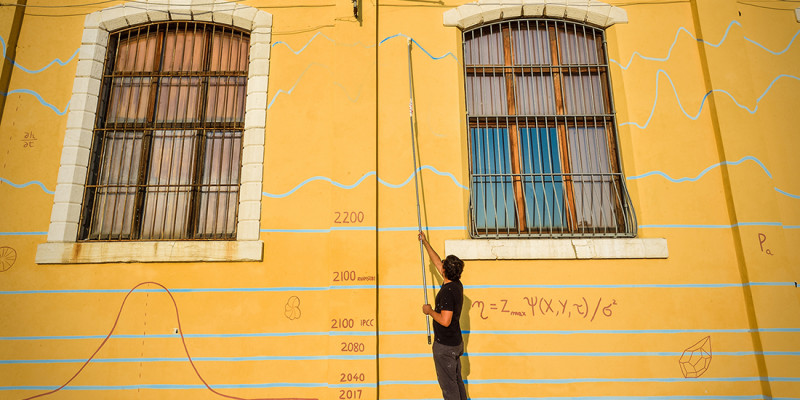 Das Foto zeigt den Künstler Andreco bei der Bemalung einer Hauswand in Venedig. Die Hauswand trägt bereits einige fiktive Hochwassermarken bis 2100. Das Bild visualisiert das Risiko des globalen Meeresspiegelanstiegs für den Menschen jenseits einer globalen Erwärmung auf 1,5 °C. 