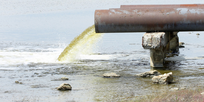 Foto: Ein Rohr, das Abwasser in einen Fluss einleitet. Im Bereich der Einleitung bildet sich Schaum.
