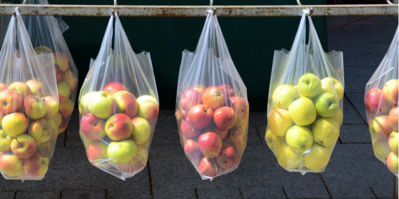 an einer Eisenstange über einem gepflasterten Platz oder Fußweg hängen durchsichtige Plastiktüten mit Äpfeln