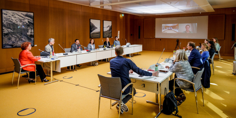 Das Bild zeigt den Raum, in welchem die Jurysitzung abgehalten wurde. Links und rechts sitzen an langen Tischen die Jurymitglieder und im vorderen Teil des Raumes wird auf einer Leinwand eine Präsentation gezeigt. 