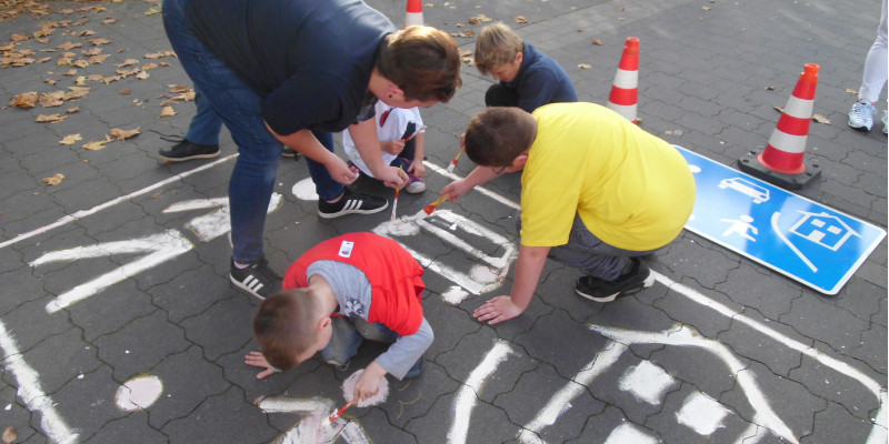Eltern und Kinder malen das Straßenschild "verkehrsberuhigter Bereich" auf den Asphalt