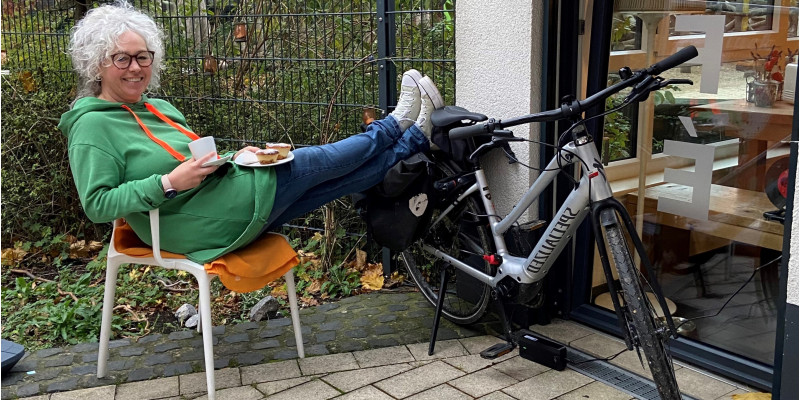 Dame sitzt mit einem Kaffee vor einem Café und lädt den Akku ihres E-Bikes