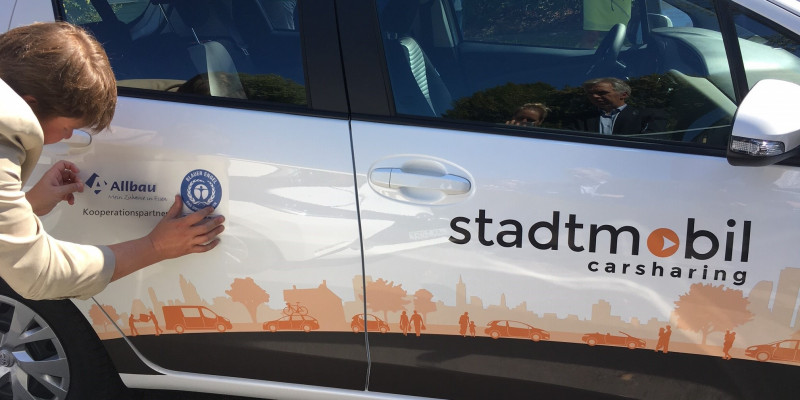 Aufkleber der Firma Allbau wird am Auto angebracht