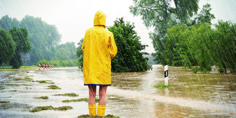 Frau steht mit Regenjacke und Gummistiefeln in einem überschwemmten Gebiet