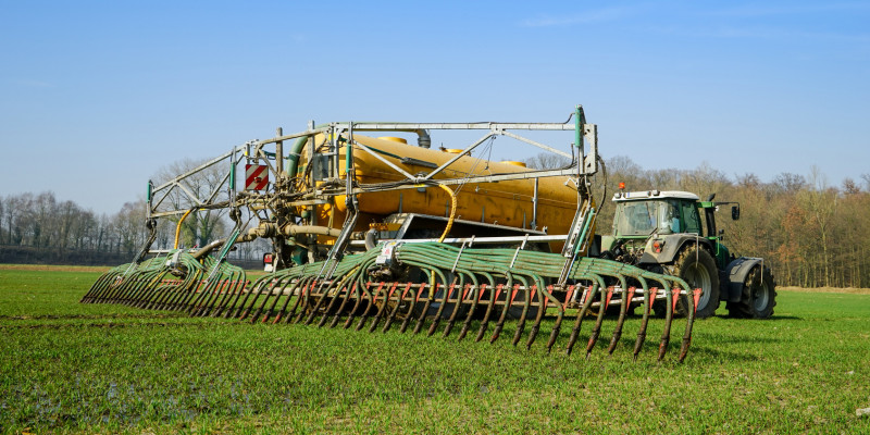 Traktor mit Gülletank und Schleppschlauch auf landwirtschaftlicher Nutzfläche 