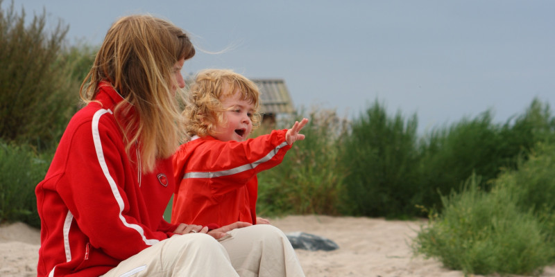 Am Strand sitzen zwei Kinder mit Regenjacken