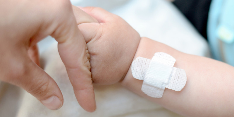 A baby hand holding the finger of an adult