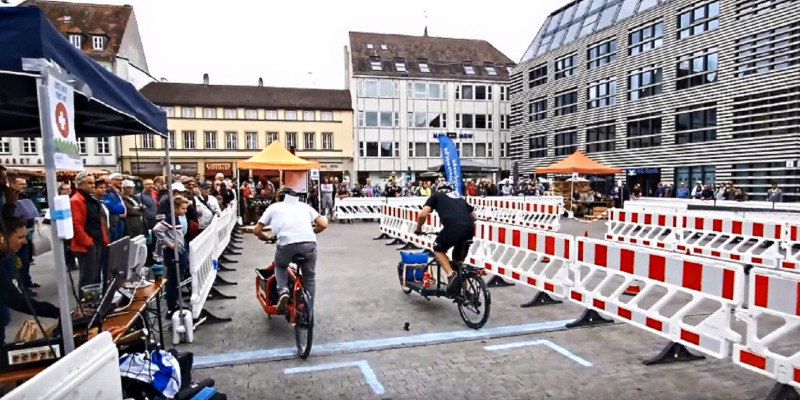 Zwei Lastenradfahrende treten auf dem Marktplatz in Würzburg gegeneinander an. Absperrung ist zu sehen. 