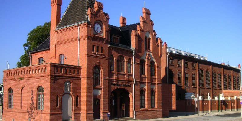 Small, old red-brick train station building with spire and gable