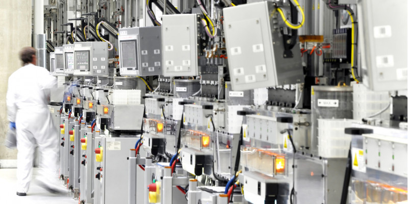 Arbeiter mit weißem Schutzanzug in der Werkhalle einer Chipfabrik mit vielen Geräten