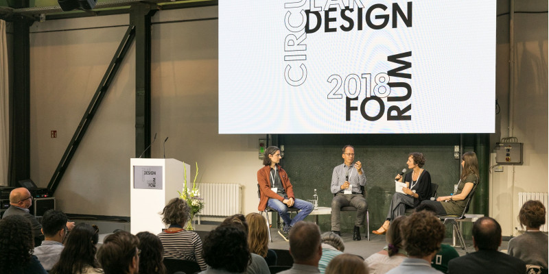 zwei Männer und zwei Frauen diskutieren mit Mikrofonen in einem Halbkreis sitzend auf einer Bühne vor Publikum, darüber ein Banner mit der Aufschrift "Circular Design Forum 2018"