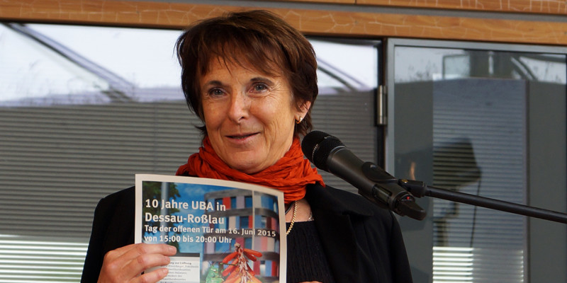 UBA-Präsidentin Maria Krautzberger am Rednerpult, sie hält ein bunt bedrucktes Blatt Papier mit dem Programm für den Tag der offenen Tür "10 Jahre UBA in Dessau-Roßlau" hoch