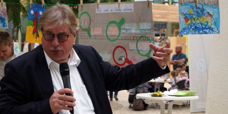 UBA-Vizepräsident Dr. Thomas Holzmann steht vor den aufgehängten Kinderbildern und spricht mit einer lebhaften Geste in ein Mikrofon