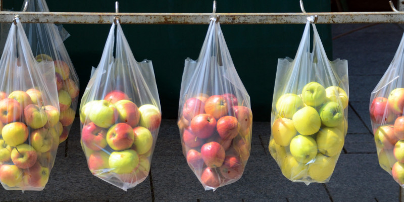 an einer Eisenstange über einem gepflasterten Platz oder Fußweg hängen durchsichtige Plastiktüten mit Äpfeln