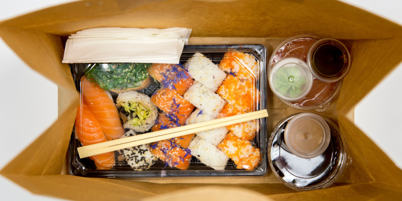 Sushi und mehrere Soßen alle einzeln in Einwegplastikbehältnissen verpackt in einer Papiertüte zum Mitnehmen