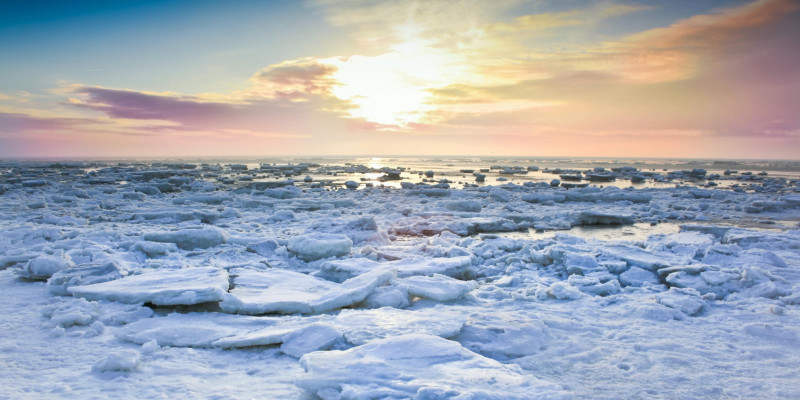 Eisschollen auf dem Meer, im Hintergrund färbt die tief stehende Sonne die Wolken am Horizont rosa