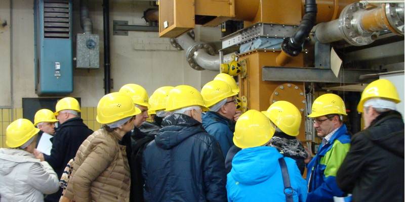 eine Gruppe Menschen mit gelben Schutzhelmen schaut sich eine technische Anlage an