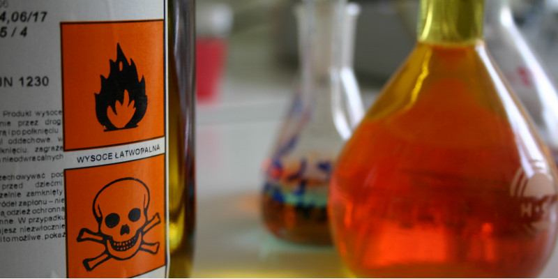 auf einem Tisch stehen Flacons mit Flüssigkeiten und eine Flasche mit Warnsymbolen "Flamme" und "Totenkopf"