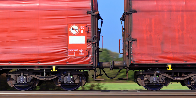 zwei rote Güter-Waggons auf der Schiene vor blauem Himmel und grüner Landschaft
