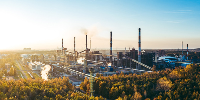 Das Bild zeigt eine Fabrik mit fünf Schornsteinen umgeben von Wald.