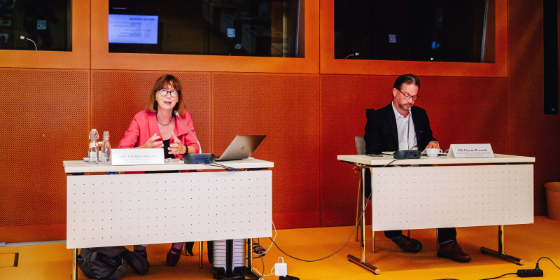 Prof. Christa Reicher und PSt Florian Pronold an jeweils einem Tisch mit Mikrofon und Namensschild