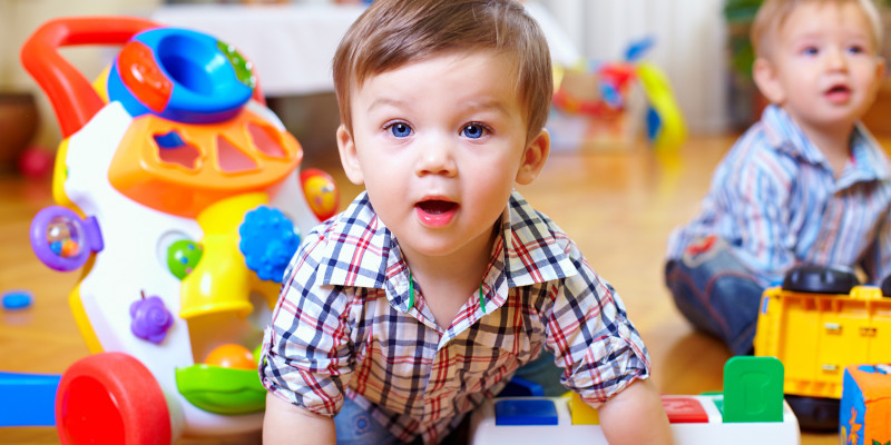 zwei Krabbelkinder spielen mit Plastikspielzeug auf dem Boden eines Raumes