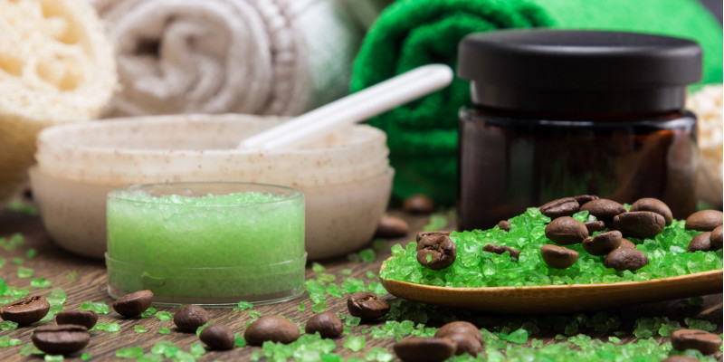 Kosmetiktiegel und Handtücher mit grünen Kügelchen und Kaffebohnen auf einer Holzoberfläche arrangiert