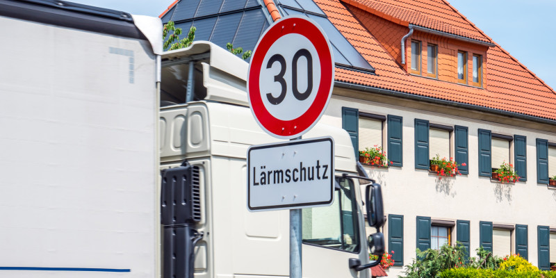 Ein Tempo 30-Schild mit Zusatzschild Lärmschutz steht an einer Stadtstraße, durch die ein Lkw fährt.