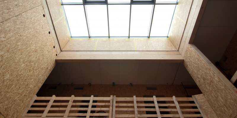 Innenansicht des Gebäudes im Rohbauzustand, die Innenwände aus rohen Holzwerkstoffplatten, durch ein Glasdacht fällt Tageslicht durch das Treppenhaus bis ins Erdgeschoss