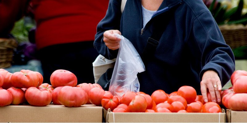 eine Kundin packt an einem Marktstand Tomaten in einen dünnen Plastikbeutel
