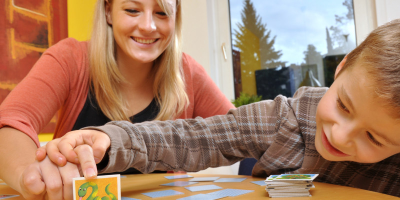 Mutter und Kind beim Memory-Spielen, die Mutter deckt ein Kärtchen mit einer Schlange auf, der Junge schaut neugierig unter die Karte, bevor sie ganz aufgedeckt ist