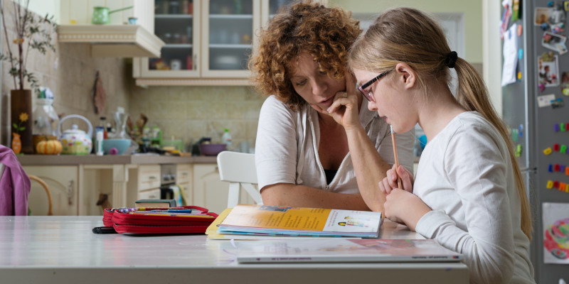 Mutter und Tochter sitzen am Küchentisch über einem Lehrbuch