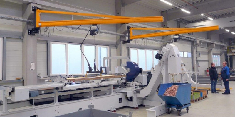 niedrige, aber breite Maschine in einer Werkshalle. Eine Metallstange ist eingespannt, Metallspäne werden in einen Rollcontainer geleitet.