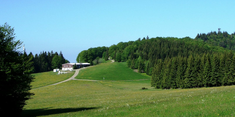 Messstationsgebäude in hügeliger Landschaft mit Wiesen und Fichtenwald