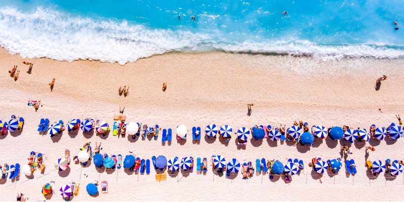 Menschen an einem Meeresstrand mit Sonnenschirmen von oben