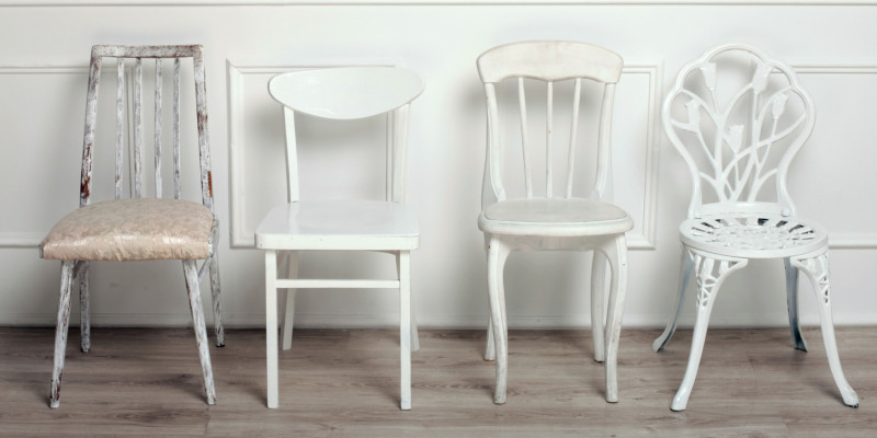 drei weiße Stühle im unterschiedlichen Stil vor einer weiß vertäfelten Wand mit Holzdielenboden