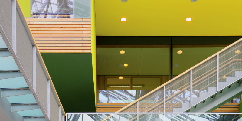 Brücken und Treppen mit gläsernen Geländern im Innenhof, Innefassade aus Holz, gelben und grünen Flächen