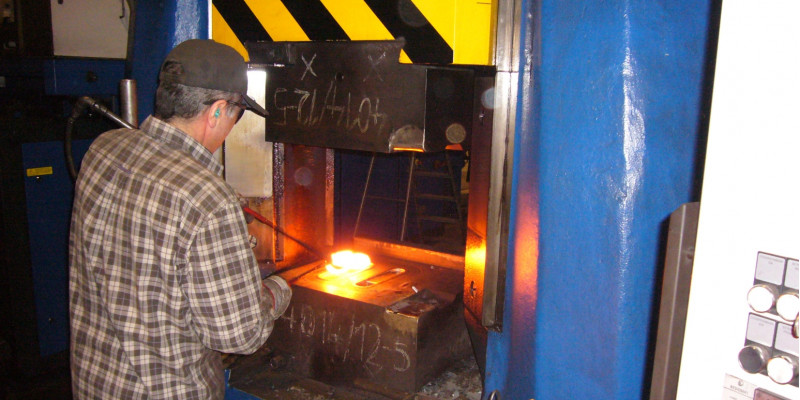 Mann arbeitet an einem glühenden Metallteil in einer Schmiedemaschine